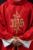Czerwony ornat liturgiczny z haftowanym motywem IHS na ozdobnej tkaninie – zbliżenie haftu