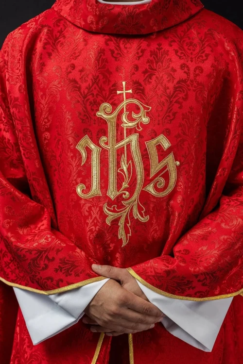 Czerwony ornat liturgiczny z haftowanym motywem IHS na ozdobnej tkaninie – zbliżenie haftu