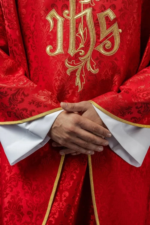 Czerwony ornat liturgiczny z haftowanym motywem IHS na ozdobnej tkaninie – detal symbolu